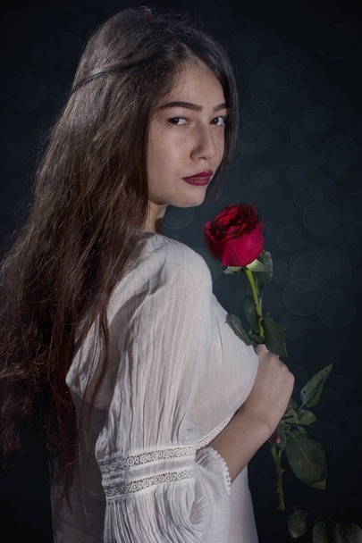 Fiatal, hosszú hajú lány pózol a fekete háttér piros rózsa - Fotó, kép