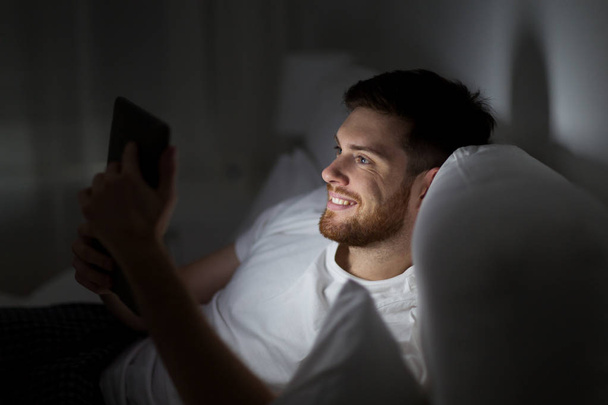 young man with tablet pc in bed at home bedroom - Foto, imagen