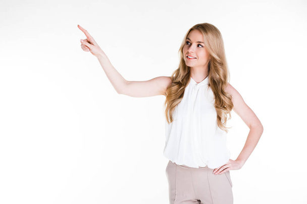 Pay attention! Beautiful young woman pointing away with smile while standing agains twhite background - Foto, afbeelding