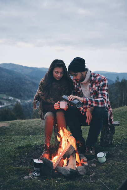 couple having coffee while spending carefree time in mountains near bonfire - Foto, Imagem