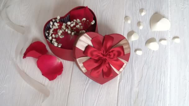 Geschenk box in vorm van hart en rood lint op houten witte achtergrond. Bovenaanzicht - Video