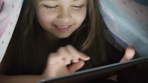 Pikkutyttö kymmenen vuotta käyttää digitaalista tablettia peiton alla, yöllä
 - Materiaali, video