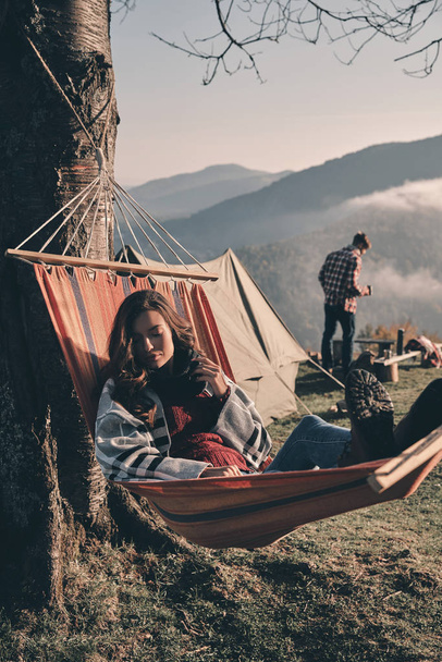 woman covered with blanket and relaxing in hammock, boyfriend standing on background  - Foto, Imagem