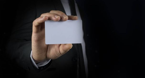 Φωτογραφία του επιχειρηματία που φοράει κοστούμι εκμετάλλευση κενή κάρτα σε μαύρο φόντο - Φωτογραφία, εικόνα