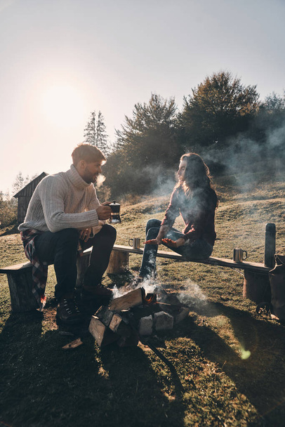 couple in love having hot drinks while spending carefree time in mountains near bonfire - Fotografie, Obrázek