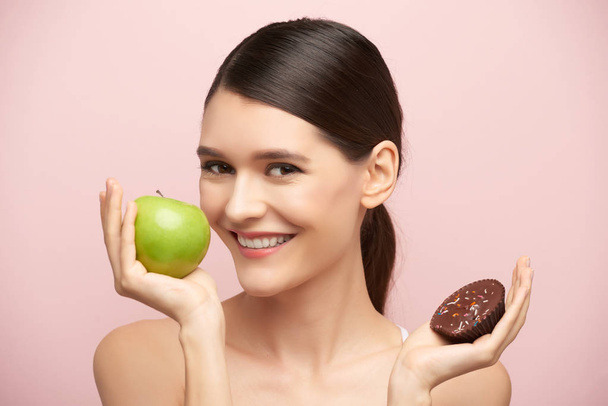 Beautiful young woman preferring apple to chocolate cake - Zdjęcie, obraz