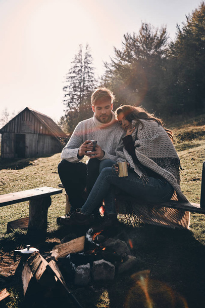 beautiful couple in love sitting on bench near bonfire in mountains - Foto, afbeelding