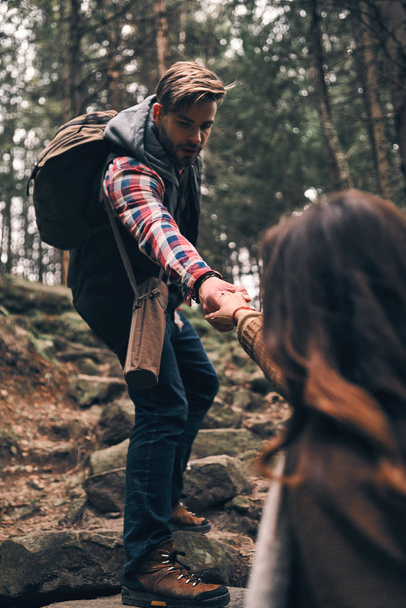 handsome man holding hands and moving up his girlfriend while hiking in mountains on rock stairs - Photo, image
