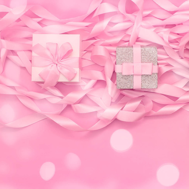 Dos cajas con regalos en el fondo de una bobina de cintas decorativas de satén de color rosa
. - Foto, imagen