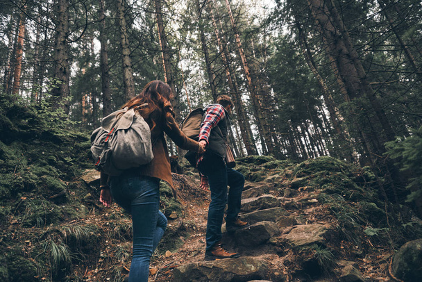 couple holding hands and moving up while hiking together in woods - Foto, afbeelding
