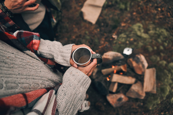 directly above shot of woman holding mug while standing in forest at campfire - 写真・画像