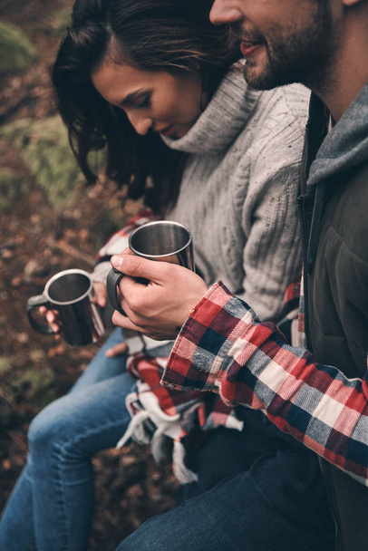 Beautiful young couple holding cups with hot drinks in forest - Zdjęcie, obraz