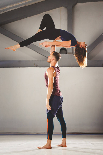 The theme of Acroyoga and Yoga Poses. A pair of two men and a woman stand in the position of asana. The guy holds the girl arched high back on the outstretched arm. In the gym with a studio Backlight - Zdjęcie, obraz