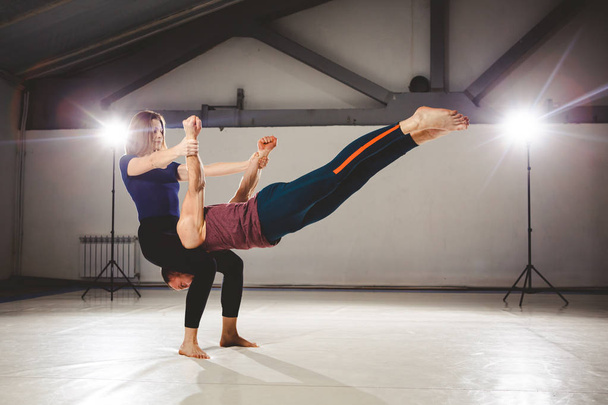 The theme of Acroyoga and Yoga Poses. Acroyogis practicing. with the studio Backlight. The woman Base keeps the man Flyer in the horizontal position Static poses - Foto, imagen