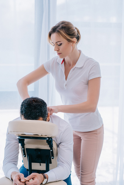 atraktivní masérka dělá ramena masáž na sedadle v kanceláři - Fotografie, Obrázek