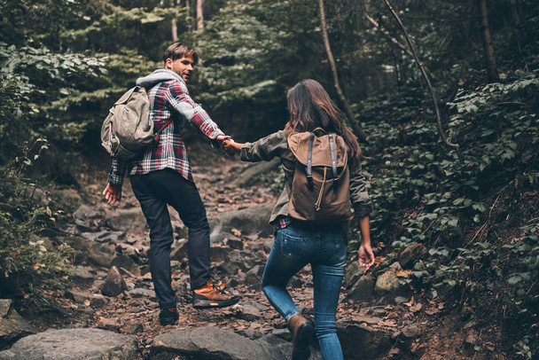 young couple holding hands and moving up while hiking together in woods - Fotografie, Obrázek