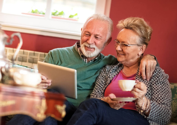 Couple using tablet at living room while drinking tea - Foto, imagen