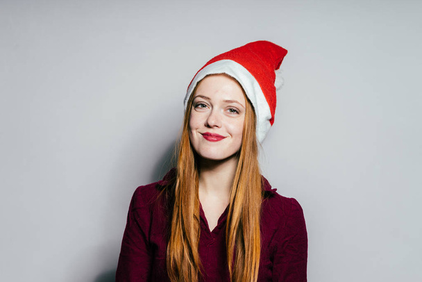happy woman in a Christmas hat on a gray background - Фото, изображение