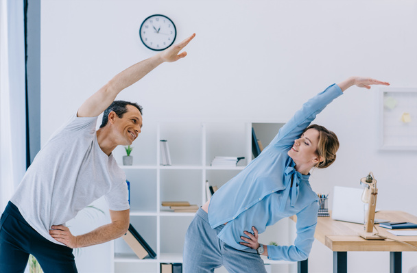 businesswoman doing side bend with trainer at office - Photo, Image