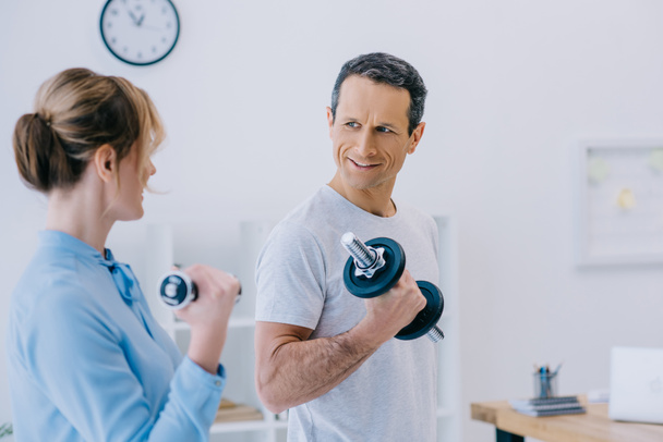 businesswoman and her handsome mature personal trainer working out with dumbbells at office - Fotografie, Obrázek