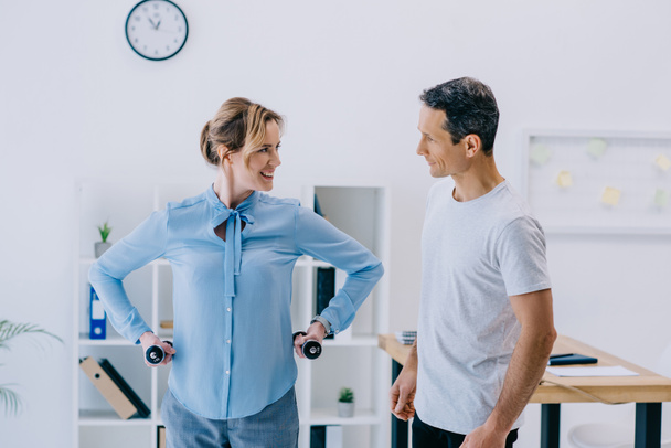 happy adult businesswoman and her personal trainer working out with dumbbells at office - Foto, Bild