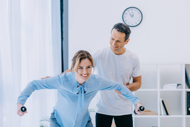 businesswoman working out with dumbbells with trainer at office - Photo, Image