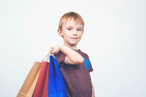 Cute happy kid with colorful shopping bags on white background. - Zdjęcie, obraz