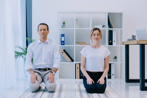 hombre de negocios guapo con su entrenador meditando en esteras de yoga en la oficina
 - Foto, Imagen