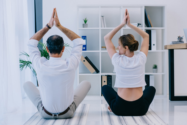 Geschäftsmann mit seinem Trainer, der im Büro in Lotus-Pose Yoga praktiziert - Foto, Bild