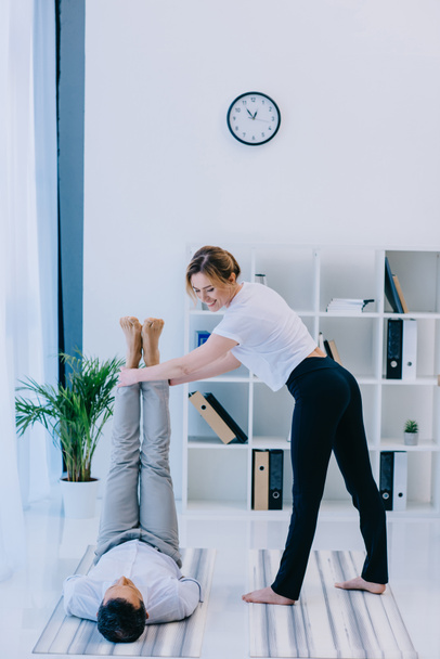 zakenman met zijn trainer praktizerende yoga in ssss vormen op kantoor - Foto, afbeelding