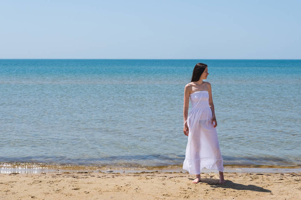 A woman in a white dress walks on the beach - Foto, Imagen