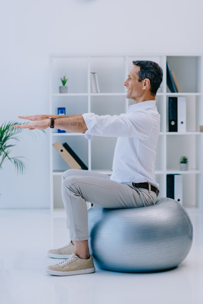 happy mature businessman balancing on fit ball at office - Photo, Image