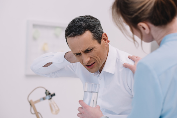 mature businessman has neck pain while his colleague trying to help him at modern office - Photo, Image