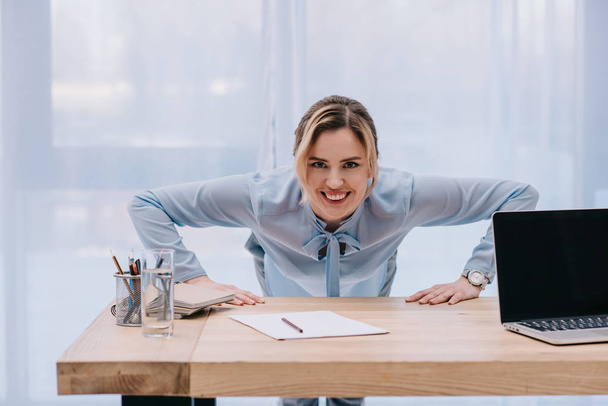 happy businesswoman doing push up on table at office - Foto, Imagen