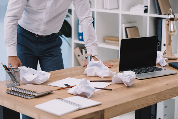 tiro cortado de empresário inclinado na mesa com papéis amassados bagunçados no escritório
 - Foto, Imagem