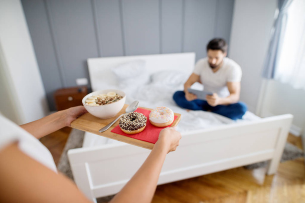 cuidado romántico joven mujer trayendo desayuno en la cama a novio en casa
  - Foto, Imagen