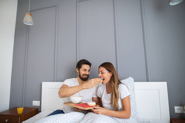 vonzó boldog fiatalember etetés barátnője az ágyban otthon - Fotó, kép