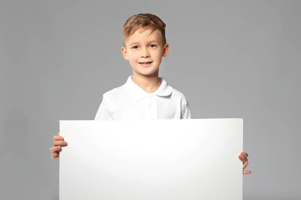 Cute boy with blank advertising board on grey background - Photo, image