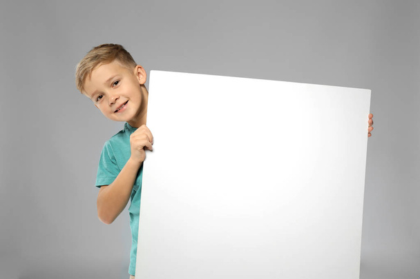 Cute boy with blank advertising board on grey background - Фото, изображение