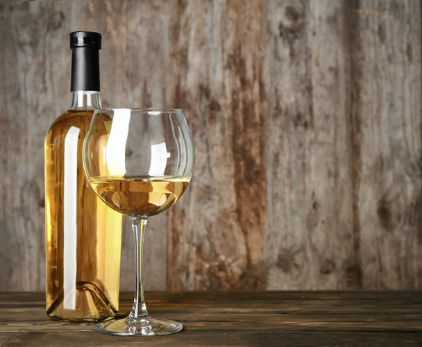 Bottle and glass with white wine on wooden table - 写真・画像