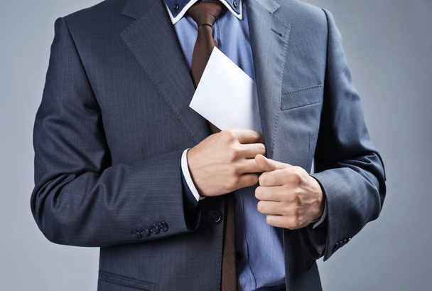 Businessman putting envelope with money in pocket on grey background. Corruption concept - Foto, Imagen