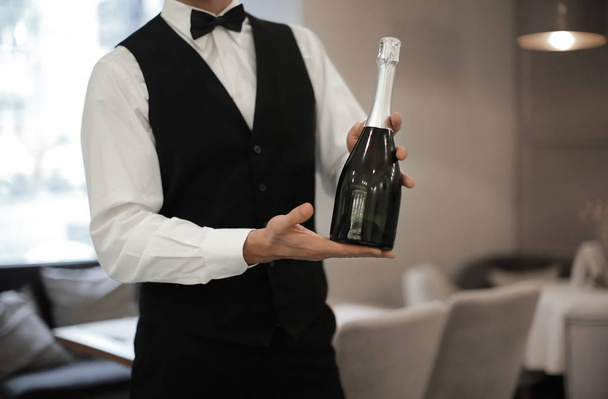 Waiter holding bottle of champagne indoors, closeup - Фото, изображение