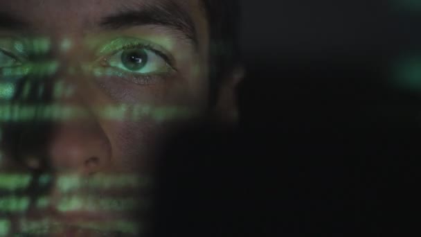 Detailní záběr muž programátor hackerům práci na počítači, zatímco zelené kód znaků odráží na jeho tvář v tmavé kanceláři místnosti. - Záběry, video
