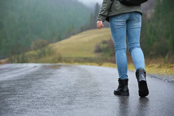 Passeggiata turistica femminile lungo la strada di campagna sotto la pioggia
 - Foto, immagini