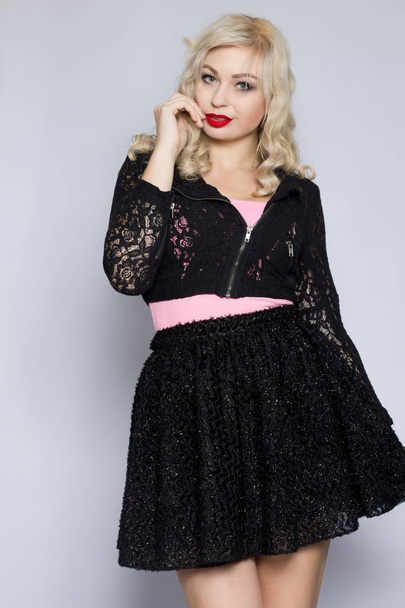 Portrait of a beautiful young blonde woman in a black lace suit. Girl posing in studio on gray background - Photo, Image