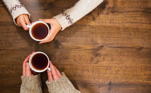 Cups of black tea in the hands of men and women. on a wooden background. with copy space. top view - Foto, afbeelding