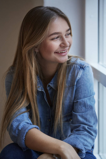Laughing girl at window in blue shirt - Valokuva, kuva
