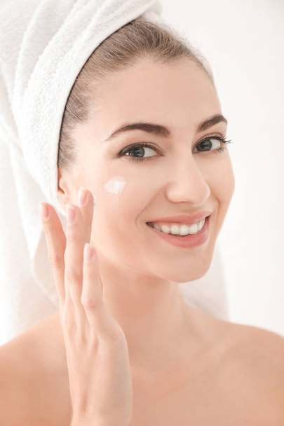Young woman applying face cream, on white background - Photo, image