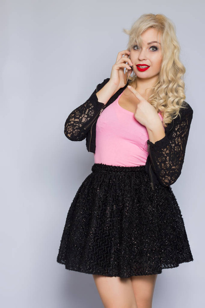 Portrait of a beautiful young blonde woman with curly hair in a black lace suit with a mobile phone in her hand - Photo, Image