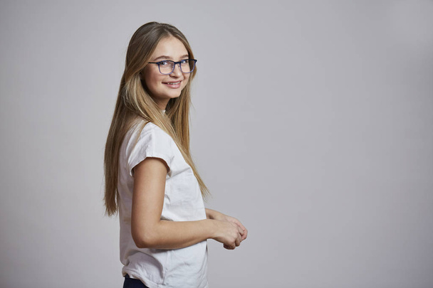 Smiling girl in glasses wearing white t-shirt turning and looking at camera - Valokuva, kuva